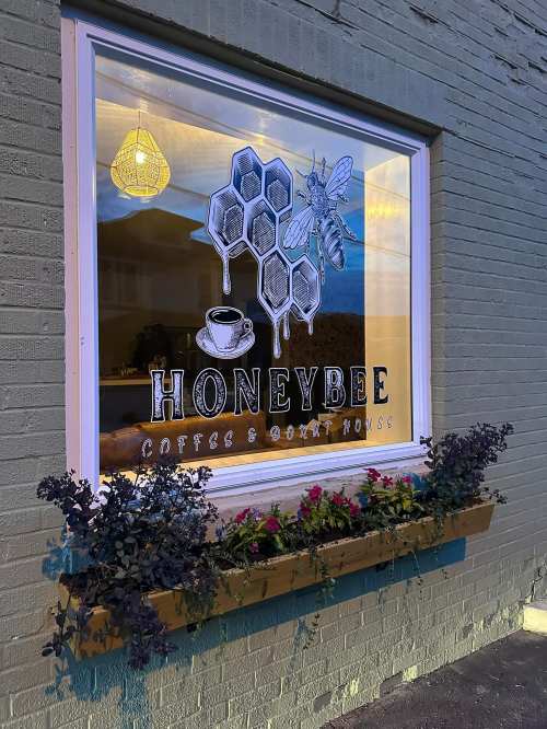 A window display featuring a honeycomb design, a coffee cup, and the name "Honeybee Coffee & Donut House."