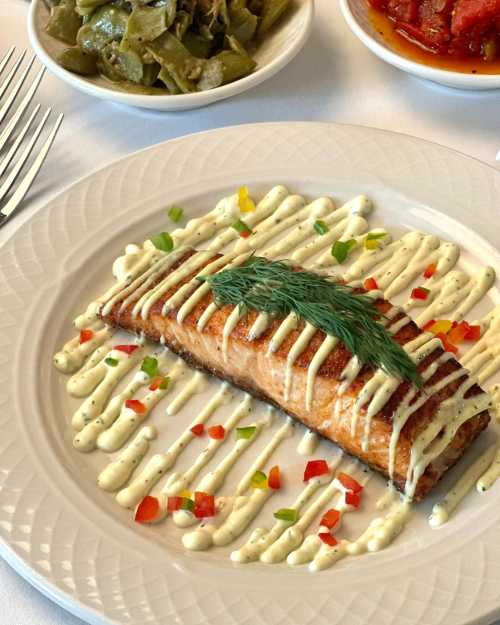 Grilled salmon fillet drizzled with sauce, garnished with dill, served with colorful pepper strips on a white plate.