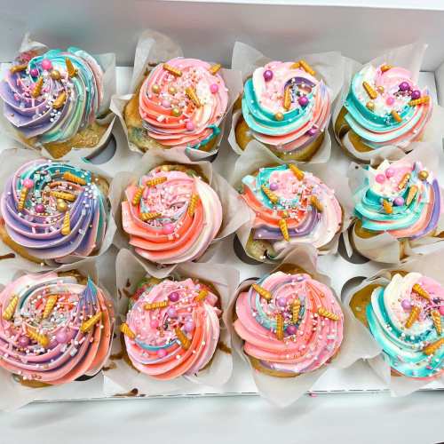 A box of colorful cupcakes with swirled frosting, sprinkles, and candy decorations.