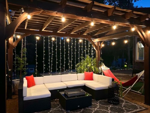 Cozy outdoor seating area with string lights, a hammock, and a coffee table under a wooden pergola at night.