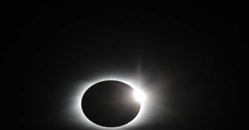 A solar eclipse with a dark moon partially covering the sun, surrounded by a bright halo of light.