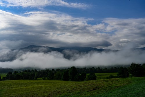 A scenic landscape featuring rolling hills, lush greenery, and misty mountains under a cloudy sky.