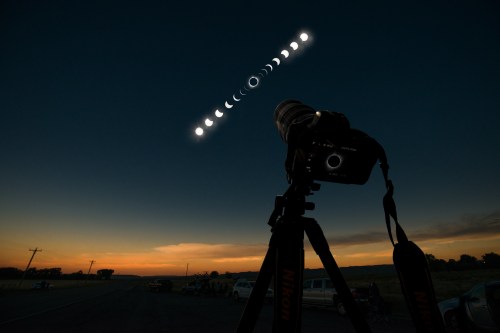 A camera on a tripod captures the phases of the moon against a twilight sky.