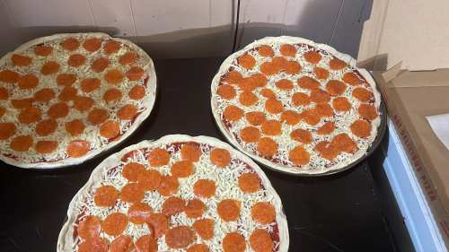 Three uncooked pizzas topped with cheese and pepperoni, placed on a black surface.
