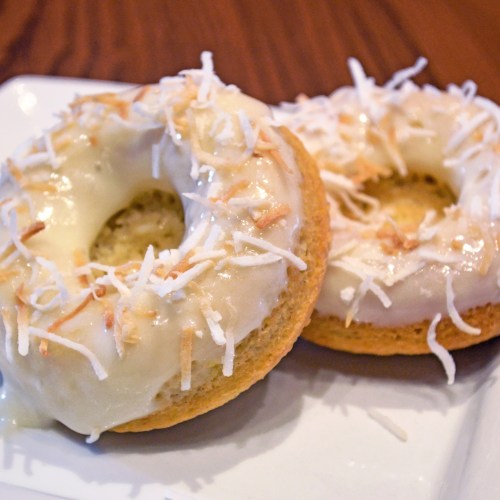 Two glazed donuts topped with shredded coconut on a white plate.