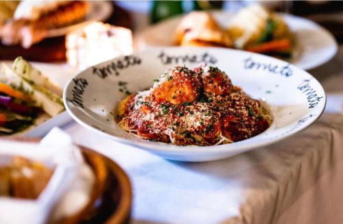 A bowl of spaghetti topped with meatballs and sprinkled with herbs and cheese, surrounded by various dishes.