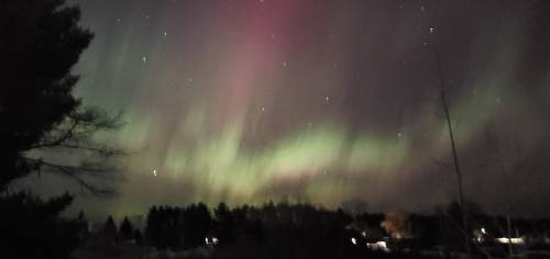 A vibrant display of the northern lights illuminates the night sky, with green and pink hues over a dark landscape.