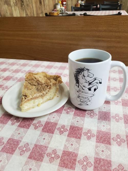 A slice of pie on a plate next to a coffee mug on a checkered tablecloth.
