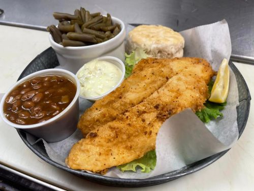 A plate with two fried fish fillets, green beans, baked beans, a biscuit, and a lemon wedge, served on lettuce.