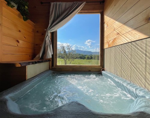 A serene hot tub with bubbling water, framed by a large window showcasing a scenic view of mountains and blue sky.