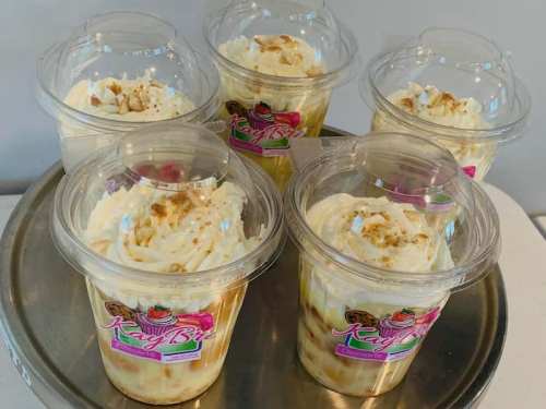 Six dessert cups with whipped cream and a graham cracker topping, displayed on a silver tray.