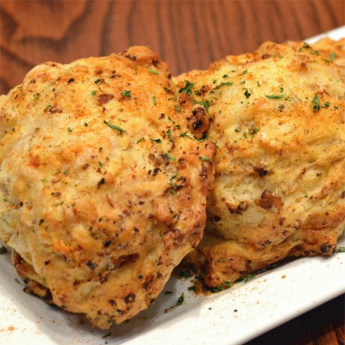 Two golden-brown, flaky biscuits topped with herbs, served on a white plate.