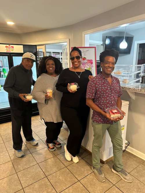 Four people stand together in a bright room, each holding a dessert cup, smiling and enjoying their time.
