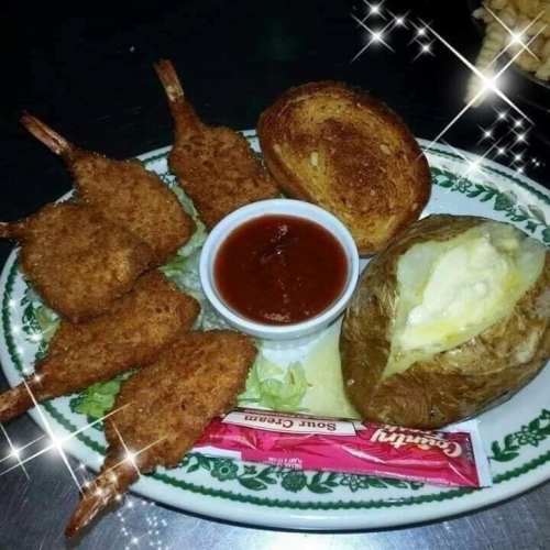 A plate featuring fried shrimp, a baked potato with sour cream, toast, and a side of dipping sauce, garnished with lettuce.