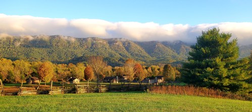 A scenic landscape featuring mountains, colorful trees, and rustic cabins under a clear blue sky with clouds.