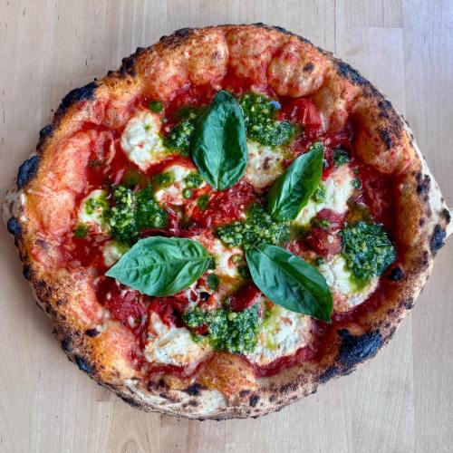 A freshly baked pizza topped with mozzarella, basil leaves, and drizzled with pesto on a charred crust.