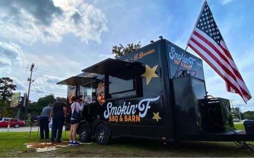 A food truck named "Smokin' F BBQ & Barn" with an American flag, serving customers outdoors.