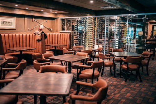 Cozy restaurant interior with wooden tables, leather chairs, and a wine display in a warm, inviting atmosphere.