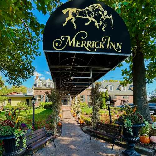 Entrance of Merrick Inn, featuring a covered walkway, colorful flowers, pumpkins, and a welcoming atmosphere.