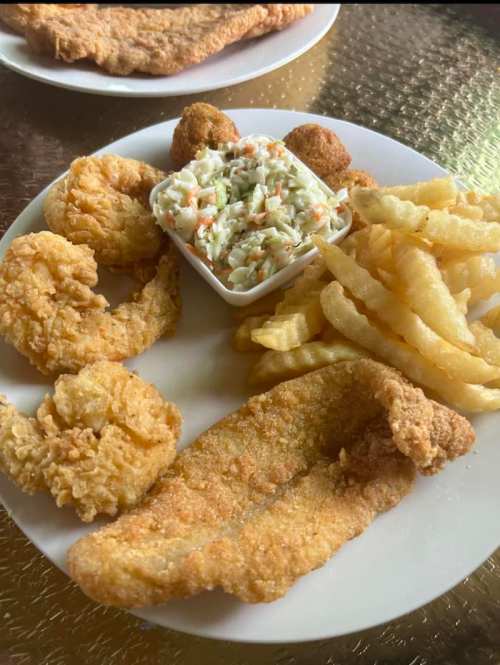 A plate of fried fish, shrimp, coleslaw, hushpuppies, and crinkle-cut fries.
