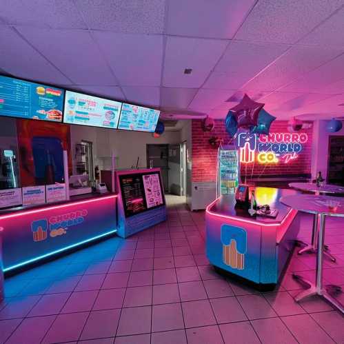 Brightly lit dessert shop interior with colorful neon signs, a counter, and tables, creating a vibrant atmosphere.