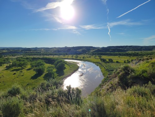 A scenic view of a winding river surrounded by lush greenery and rolling hills under a bright blue sky.