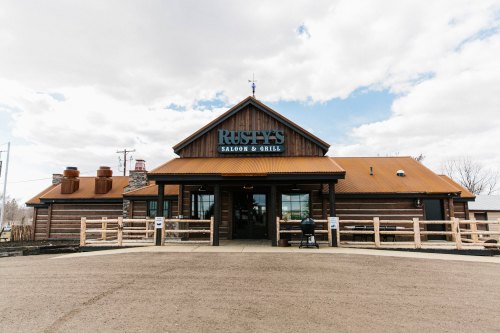 Exterior of Rusty's Saloon & Grill, a wooden building with a metal roof, under a cloudy sky.