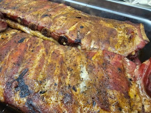 Close-up of two large, seasoned racks of ribs, cooked to a golden brown with a smoky char.