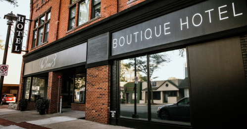 Exterior of a boutique hotel with large windows and a sign, featuring brick architecture and nearby street view.