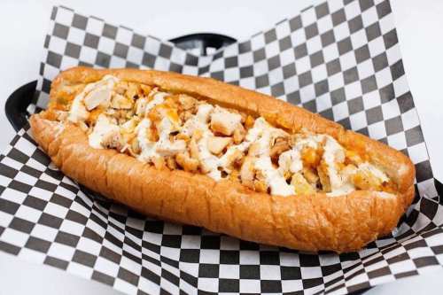 A loaded sandwich in a checkered paper, featuring shredded chicken and creamy sauce in a soft, toasted bun.