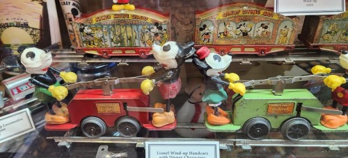 Vintage wind-up toys featuring Mickey and Minnie Mouse, pulling colorful train cars in a display case.