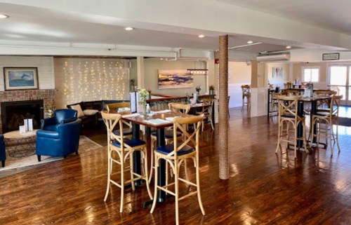 A cozy restaurant interior with wooden floors, tables, and a fireplace, featuring soft lighting and a welcoming atmosphere.