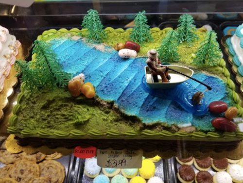 A colorful cake featuring a blue river, trees, and a figurine in a boat, priced at $31.99.