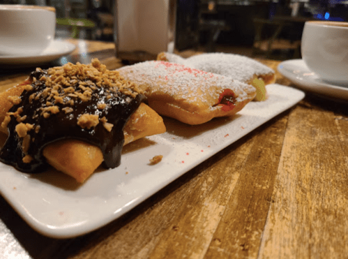 A plate of pastries filled with chocolate and fruit, topped with crushed nuts and powdered sugar, on a wooden table.