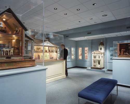 A museum exhibit featuring detailed miniature houses and a visitor observing the displays in a well-lit gallery.