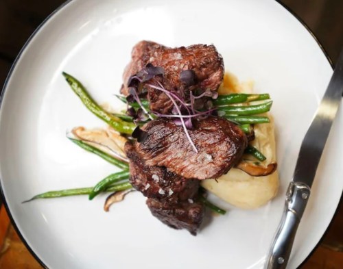 A plate of grilled steak served with green beans and creamy mashed potatoes, garnished with microgreens.