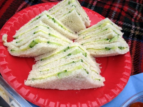 A red plate with neatly cut cucumber sandwiches stacked in a triangular arrangement.