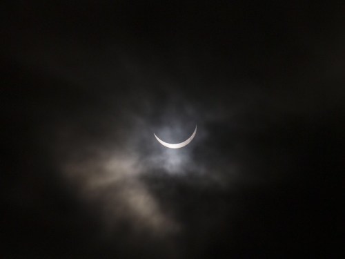 A crescent moon partially obscured by dark clouds in a night sky.