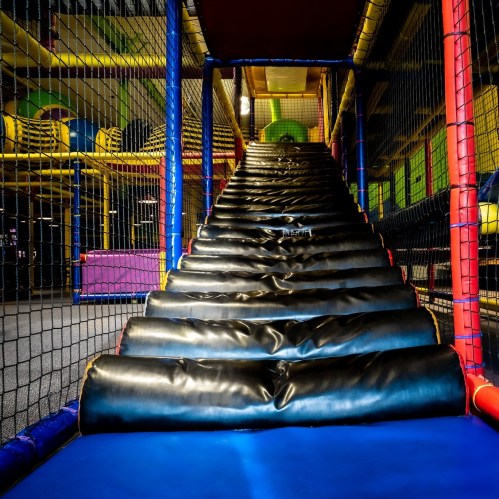 A colorful indoor play area featuring a large, padded slide leading up to a play structure.