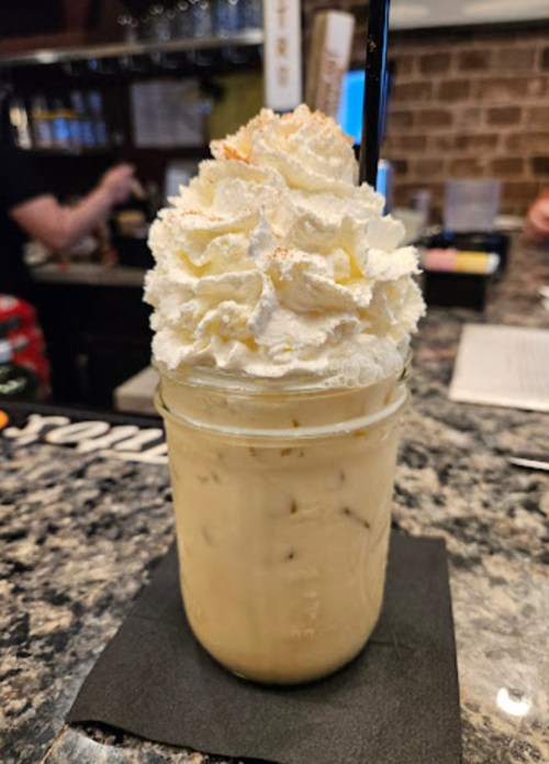 A creamy drink topped with whipped cream, served in a mason jar on a black napkin, with a straw.