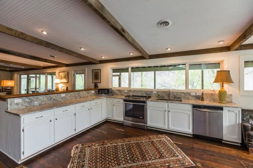 Bright kitchen with white cabinets, granite countertops, stainless steel appliances, and a cozy rug on dark wooden floors.