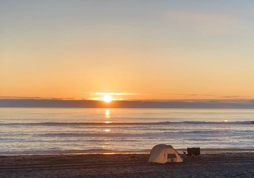 A serene beach at sunset with a tent and calm waves reflecting the orange and pink sky.