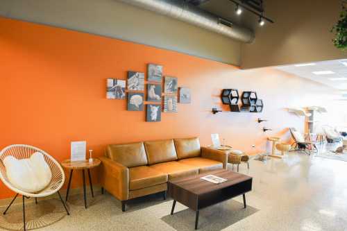 A cozy lounge area with an orange wall, featuring a brown sofa, coffee table, and decorative wall art.