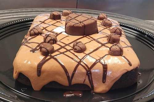 A square chocolate cake topped with creamy chocolate frosting and decorated with chocolate pieces and drizzles.