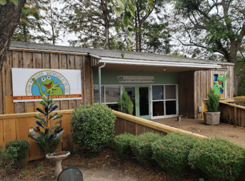A wooden building with green accents and a frog logo, surrounded by trees and landscaping.