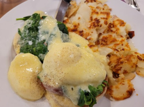 A plate of eggs Benedict with spinach and hollandaise sauce, served alongside crispy hash browns.