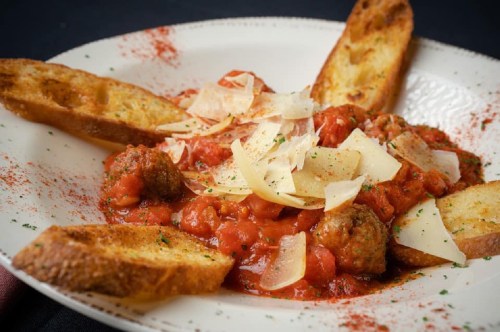 A plate of meatballs in marinara sauce, topped with cheese shavings, accompanied by toasted bread slices.