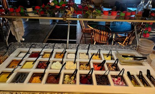 A buffet-style salad bar with various toppings, including vegetables, cheeses, and dressings, arranged in containers.