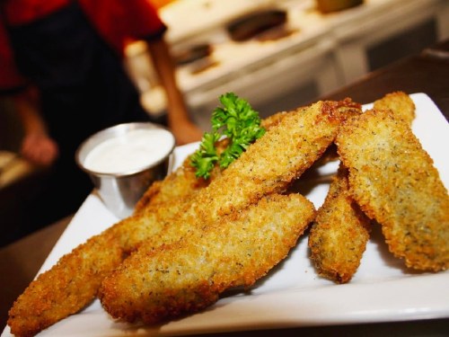 A plate of golden-brown fried zucchini sticks served with a side of dipping sauce and garnished with parsley.