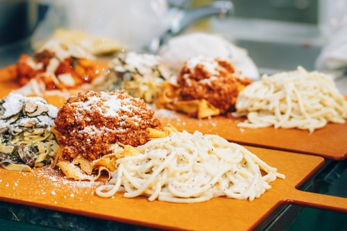 Three plates of pasta with different sauces, including a meat sauce and creamy white sauce, garnished with cheese.